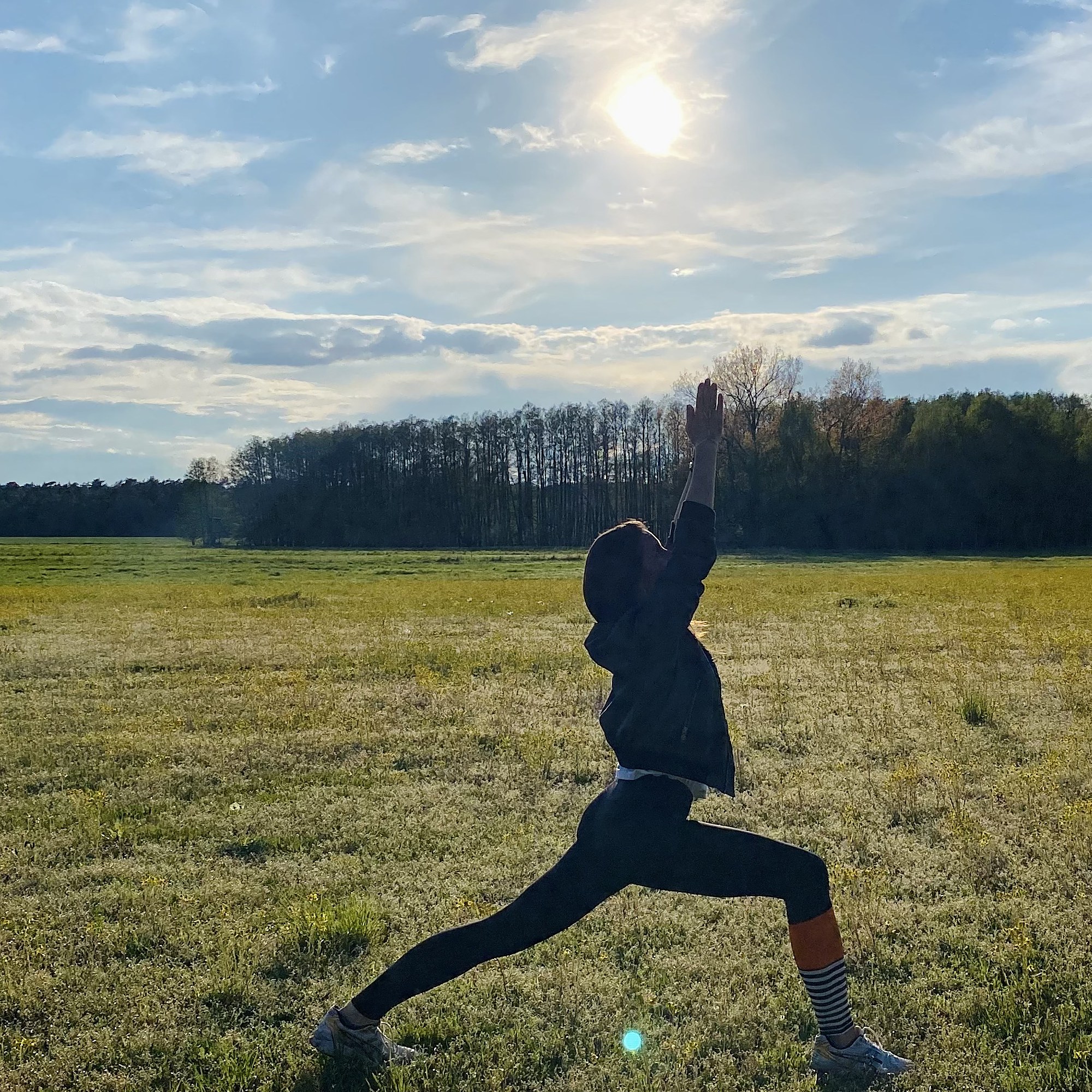 Andrea Foth in a lunging yoga pose reaching toward the rising sun in an open field.